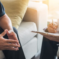 Doctor consulting male patient, working on diagnostic examination on men's health disease or mental illness, while writing on prescription record information document in clinic or hospital office